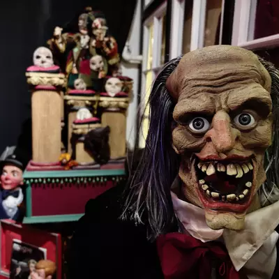 Close-up of a grotesque carnival puppet head with exaggerated features, bulging eyes, prominent teeth, and long dark hair, part of the puppet collection at Dreamfactory museum in Degersheim
