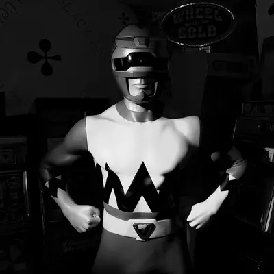 Mannequin figure wearing a silver Power Ranger helmet and costume with white top and black zigzag pattern, displayed in museum arcade section with 'Wheel of Gold' signage visible at Dreamfactory museum in Degersheim