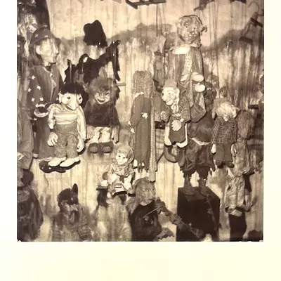 Black and white Polaroid showing numerous antique marionette puppets hanging from strings, displaying various character types including children, elderly figures, and theatrical characters at Dreamfactory museum in Degersheim