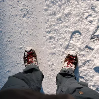 First-person view of hiking boots standing on fresh snow with footprints