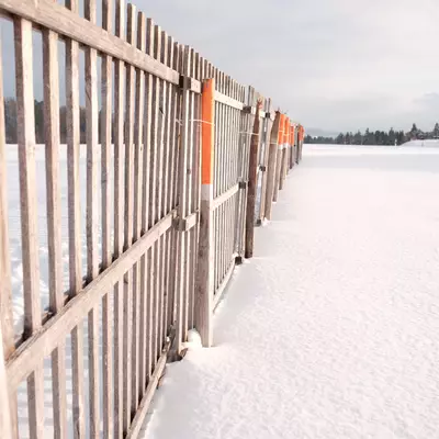 Wooden safety barrier with orange flags along a snow-covered field