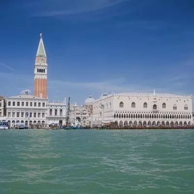 Venice waterfront skyline seen from the water, showing the Campanile di San Marco, the Doge's Palace and surrounding buildings under a bright blue sky