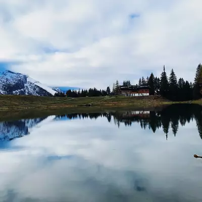 le lac Reto est au premier plan. On peut voir le restaurant sur l'autre rive. Le ciel et les nuages se réfléchissent à la surface du lac.