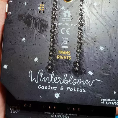 Close-up of a black electronic device or circuit board held in someone's hand, decorated with white snowflake designs and cursive text reading 