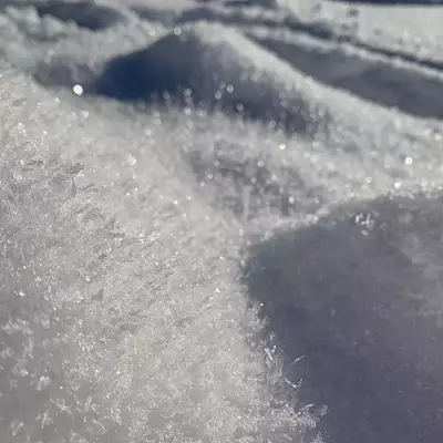 Close-up of snow and ice crystals with sparkling texture, featuring dark shadowed areas and bright crystalline surfaces catching light.