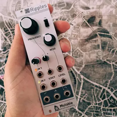 A hand holds a white Eurorack synthesizer module labeled 