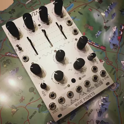 A white synthesizer module with multiple black knobs and sliders arranged in rows, featuring jack sockets at the bottom labeled 