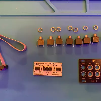 Electronic components laid out on a blue surface including seven brown cylindrical capacitors with gold rings, a rainbow-striped cable, a tan circuit board with integrated circuits, and a brown module with labeled terminals and circular components.