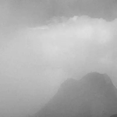 A monochrome image capturing the silhouette of an ibex on the ridge of a mist-covered mountain at Grand Chamossaire, with clouds enveloping the peak.