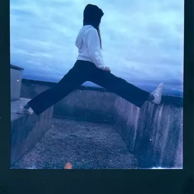 Person jumping with legs spread wide against a concrete wall at dusk in Nyon, with cloudy evening sky in the background