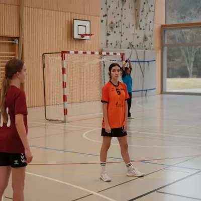 Joueuse du TV Birsfelden en bordeaux et joueuse du HBC Moudon en orange se faisant face sur le terrain, près du but, pendant une pause de jeu