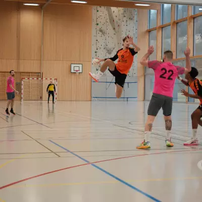 Joueur numéro 9 du HBC Moudon en orange sautant pour tirer, face aux défenseurs du RSB/Yverdon numéro 22 en rose tentant de bloquer