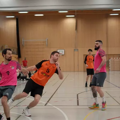 Joueur numéro 5 du HBC Moudon en orange poursuivant un joueur du RSB/Yverdon numéro 9 en rose qui porte le ballon