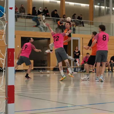 Joueur du HBC Moudon tirant derrière les défenseurs du RSB/Yverdon numéros 9 et 22 en rose, face au gardien en bleu et au public dans les tribunes