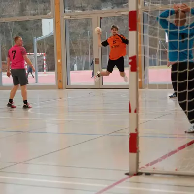 Joueur numéro 8 du HBC Moudon en orange tirant au but, avec un joueur du RSB/Yverdon numéro 7 en rose et le gardien en bleu