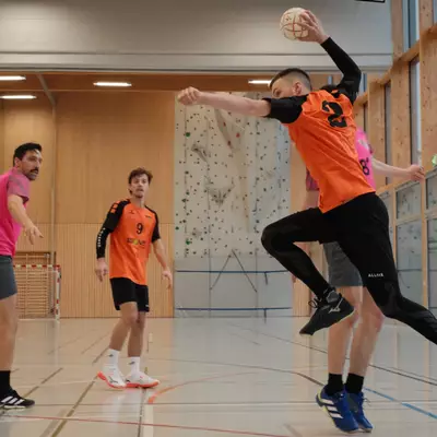 Joueur numéro 2 du HBC Moudon en orange armant un tir puissant, avec un coéquipier numéro 9 et un défenseur du RSB/Yverdon en rose