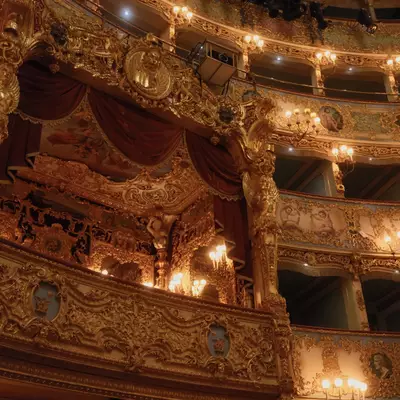 Interior of Teatro La Fenice opera house in Venice, ornate gilded boxes and balconies with red velvet drapes illuminated by warm chandeliers