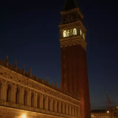 Piazza San Marco at night, the illuminated Campanile di San Marco towering above the arcaded Procuratie, warm lamp light over the square and its visitors
