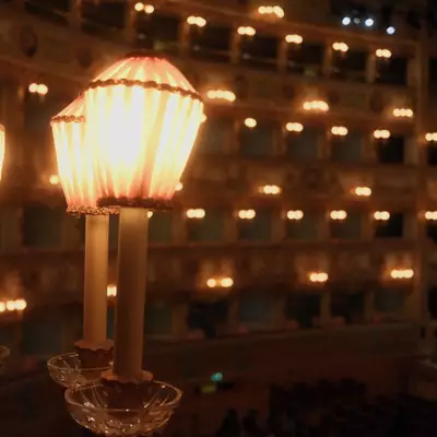 Two lit candelabras in the foreground with the blurred illuminated tiers of La Fenice opera house balconies glowing warmly behind them