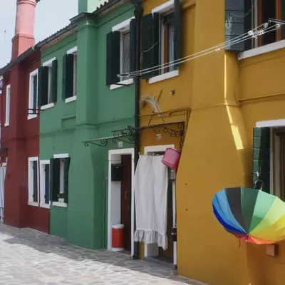 Row of colourful houses in Burano with a rainbow umbrella hanging on a yellow facade, laundry and curtains drying outside