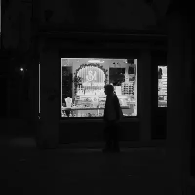 Silhouette of a person standing in front of an illuminated jewellery shop window at night, black and white