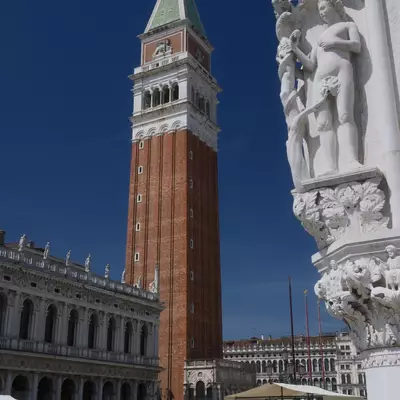 The Campanile di San Marco seen from Piazza San Marco, with ornate marble carvings of the Doge's Palace in the foreground and tourists and market stalls below