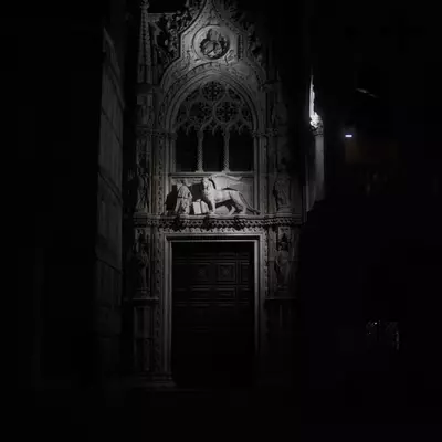 Gothic stone portal of the Doge's Palace at night, a spotlight on a winged lion of Saint Mark relief sculpture above the doorway, darkness surrounding
