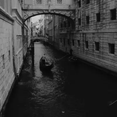 Black and white view of the Bridge of Sighs over a Venetian canal, a gondolier steering his boat beneath it
