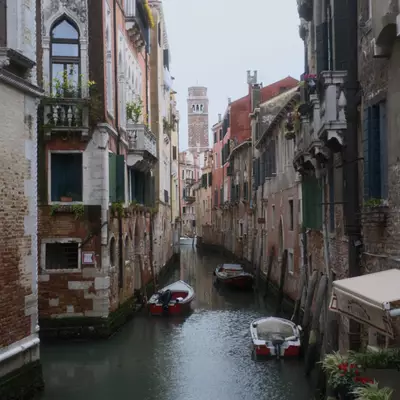 Quiet Venetian canal flanked by colourful historic buildings with balconies and flowers, small boats moored on both sides, a campanile visible in the background