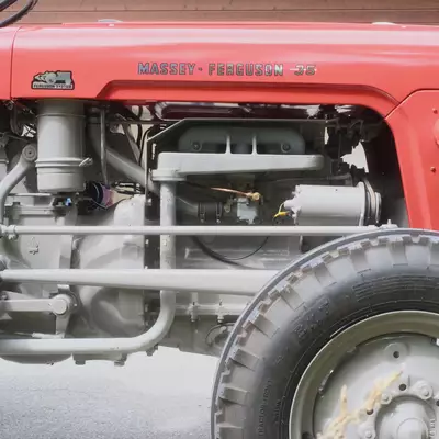 Close-up side view of a vintage red Massey-Ferguson 35 tractor, showing its engine bay and large rear tyre in front of a wooden chalet wall.