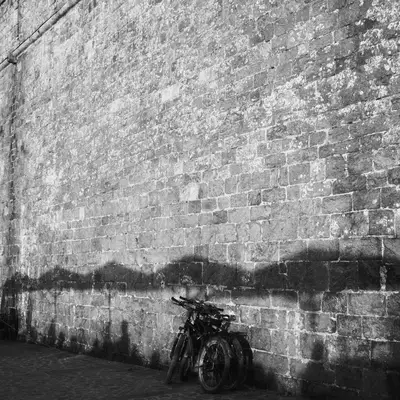 A bicycle leaning against the ramparts wall of Saint-Malo, where the shadows of a café terrace’s umbrellas are outlined.