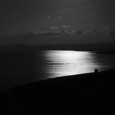 View of Lake Geneva from the terraces of Lavaux. The image is in black and white. You can make out the silhouettes of boats standing out against the water lit by the sun.