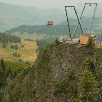 The V-shaped structure of the Balanc'Air at Grand Chamossaire in Villars, with a group of riders launched into the void facing the Alpine panorama. Visitors wait on the wooden platform.