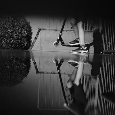 A skateboarder reflected in wet pavement at the skatepark.