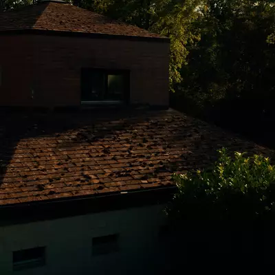 A brick clubhouse with a shingled roof glows in evening light, surrounded by dense trees and shrubs.