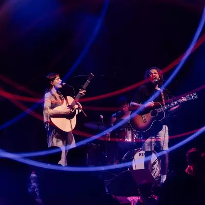 Two musicians from Stain of Light are playing guitar on stage, surrounded by blue and red light trails.