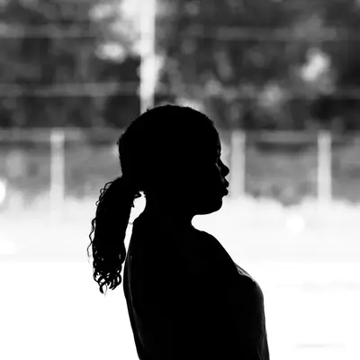 Silhouette of a person with curly hair tied up, seen in profile, against a blurred black and white background.