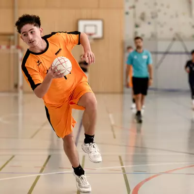 A player in an orange shirt runs with the ball during a handball match.