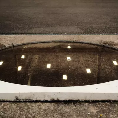 Circular shot put ring filled with water, reflecting rows of ceiling lights, with a white curb along its edge.