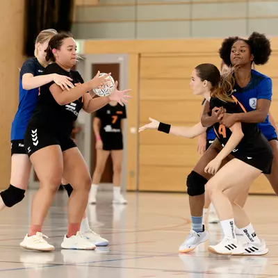 Joueuses de handball en action sur le terrain, l'équipe de Moudon en noir affrontant Crissier en bleu, ballon en jeu.
