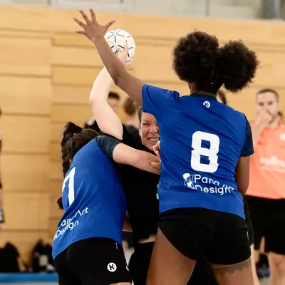 Joueuses de handball en maillot bleu (Crissier) sautant pour intercepter un ballon, face à une adversaire en noir (Moudon).
