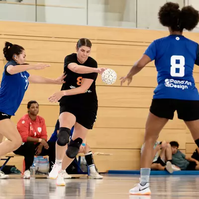 A player from Moudon (in black) holds the ball while a Crissier player (in blue) attempts to block her during a match.