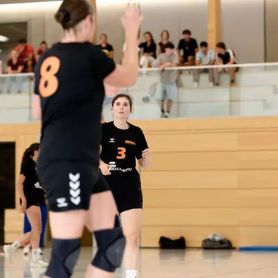 Joueuses de handball en maillot noir portant les numéros 8 et 3 sur le terrain, avec des spectateurs en fond.