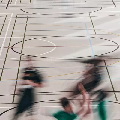 Goalkeeper standing near the goal on an indoor court while blurred players move quickly in the foreground, showing motion.