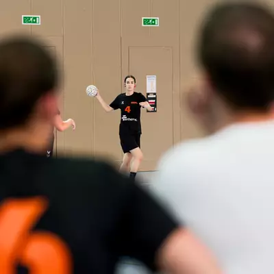 Handball player in black jersey number 4 holding the ball, facing two blurred teammates in the foreground.