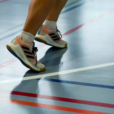 Close-up of a person's legs and sneakers on a gymnasium floor with colored court lines, mid-stride during a match.