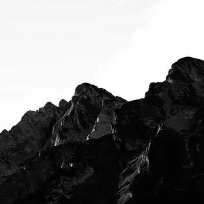 Black silhouette of a jagged mountain ridge against a white sky, near La Clusaz.