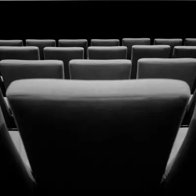 Rows of empty cinema seats face a blank screen, photographed in black and white with no audience present.