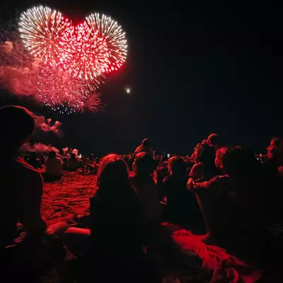 Children watching a firework display. Three red rockets explode in the sky.