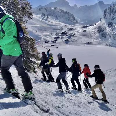 Yann, Annick, Pierre-Yves, Vania, Natacha, Annick, Christophe, Cédric and Céline pose in their ski clothes on the piste. In the background we see the Brettaye train station and the lake covered with snow